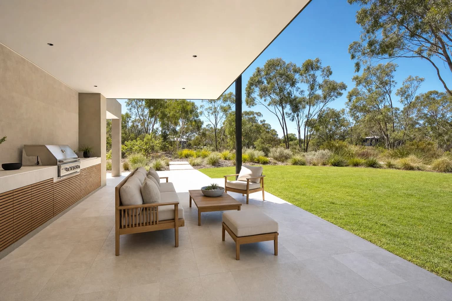 Pale porcelain alfresco paving under a flat patio roof running out past the roofline onto a sunlit lawn