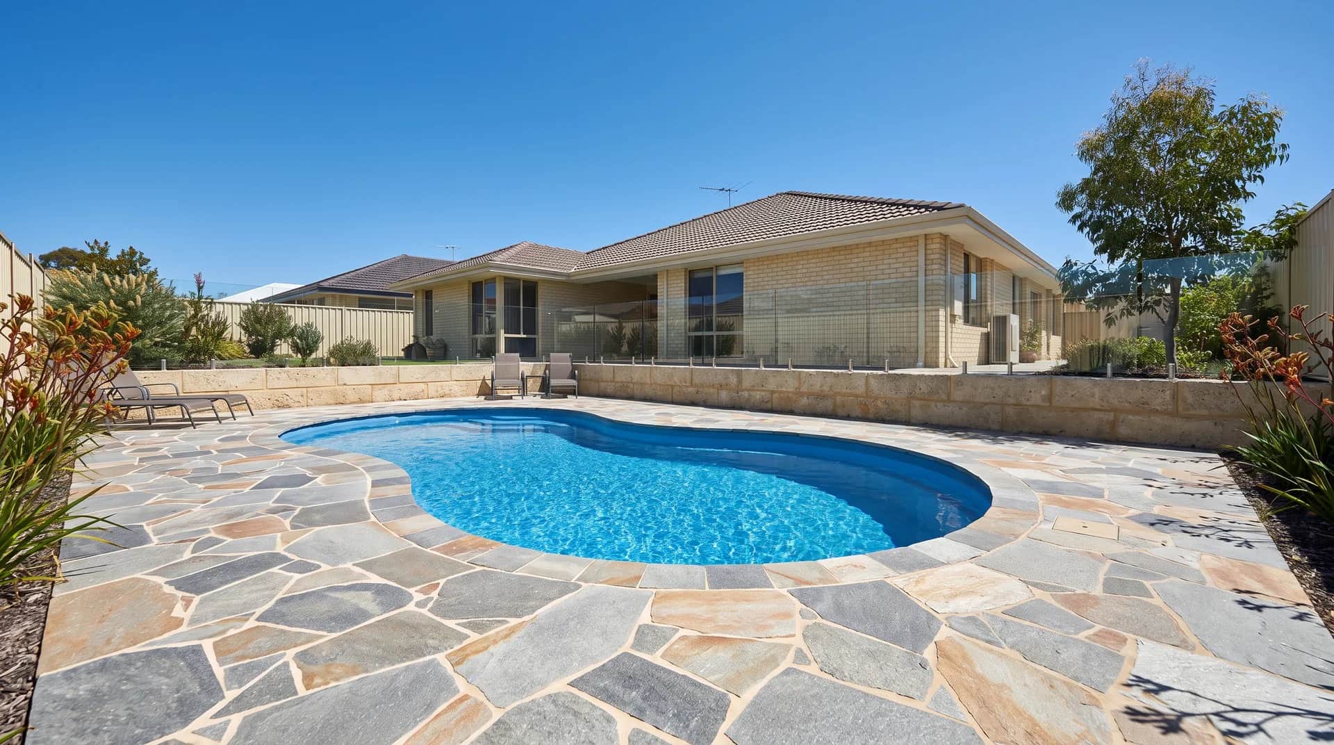 Crazy paving in grey and tan natural stone laid around a freeform kidney pool at a Perth home, cut and fitted with narrow grouted joints