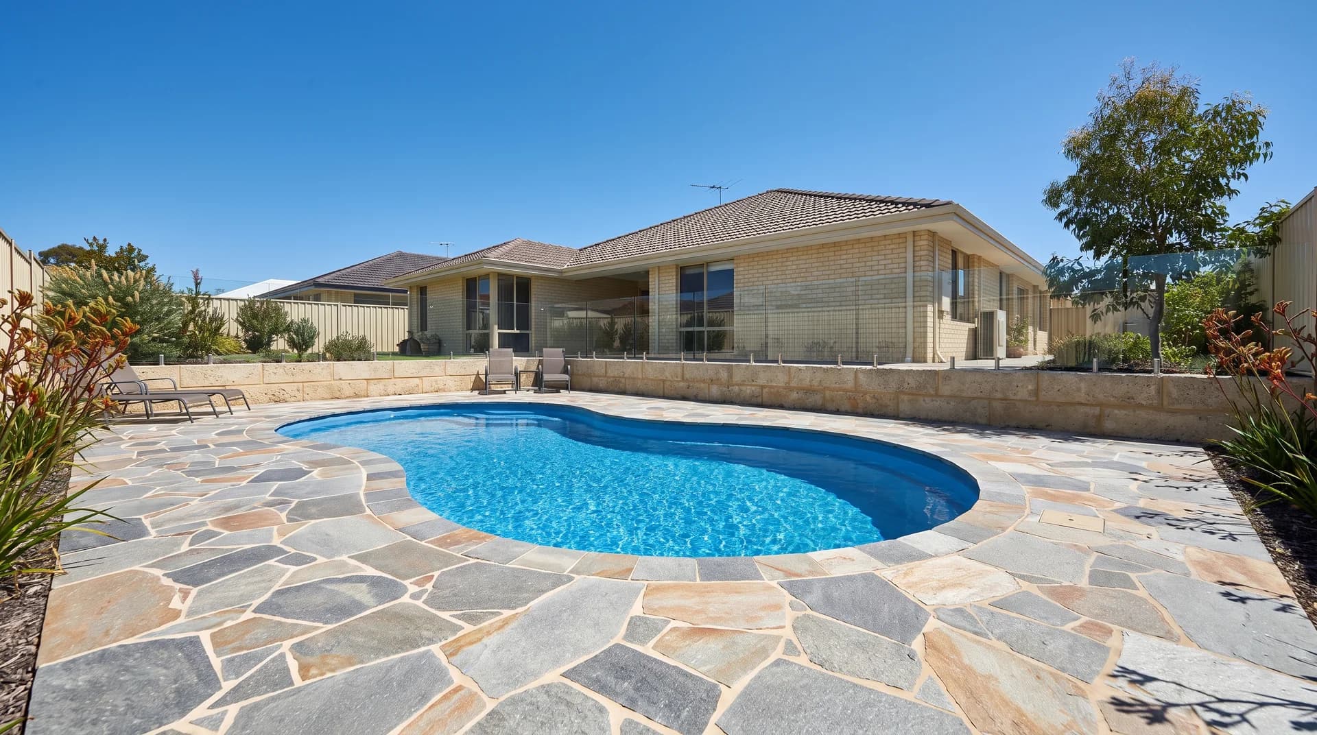 Crazy paving in grey and tan natural stone laid around a freeform kidney pool at a Perth home, cut and fitted with narrow grouted joints