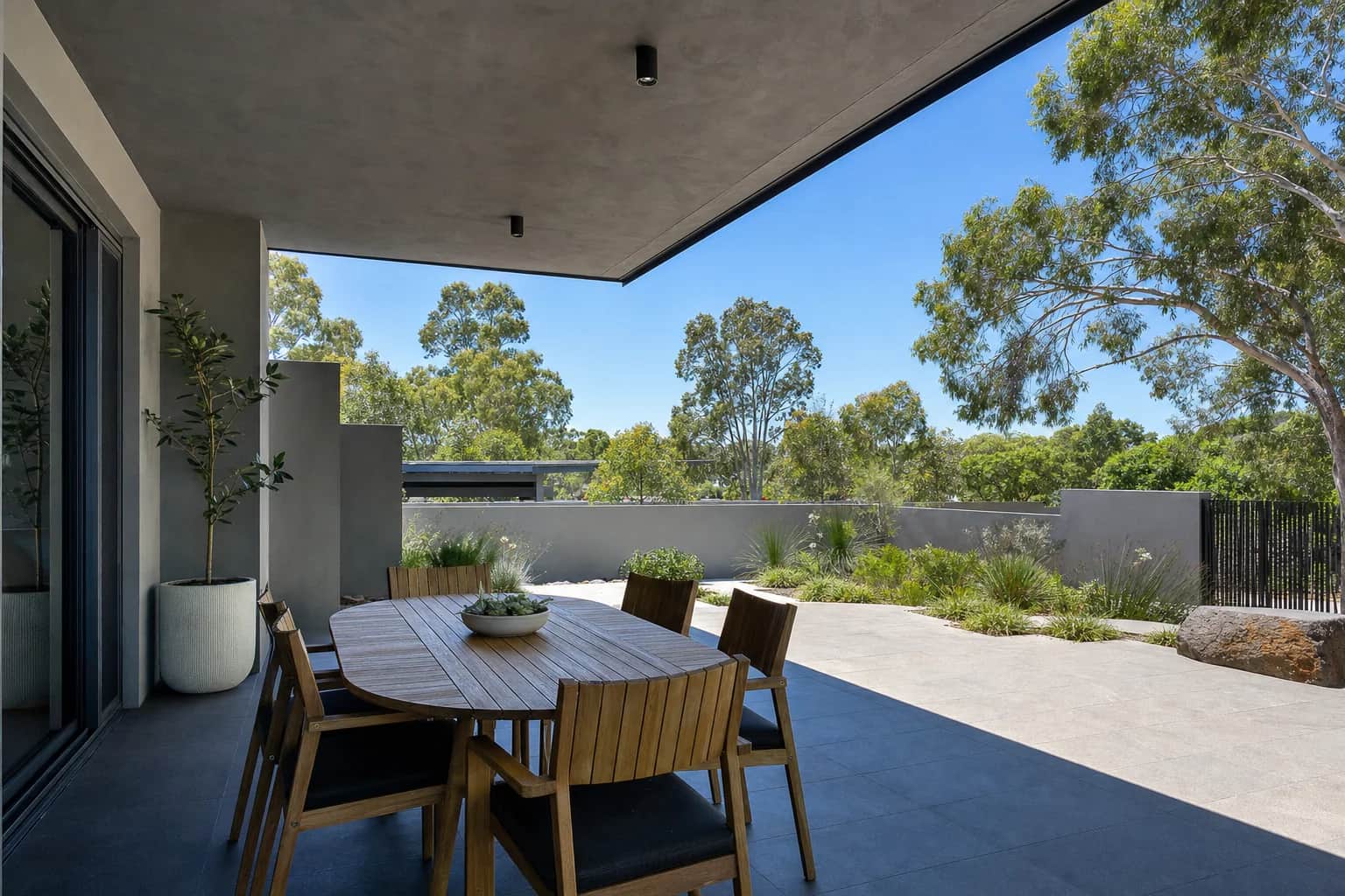 A covered alfresco paved in dark charcoal porcelain looking out to bright paving and garden beyond