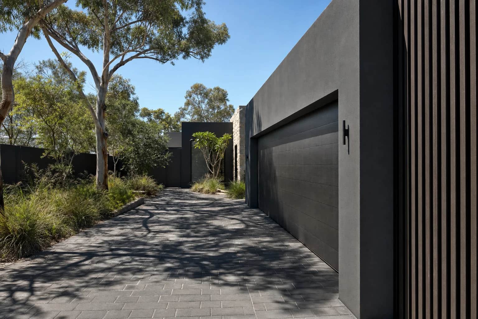 Dark charcoal stone driveway paving beside a charcoal rendered garage wall and timber batten screen