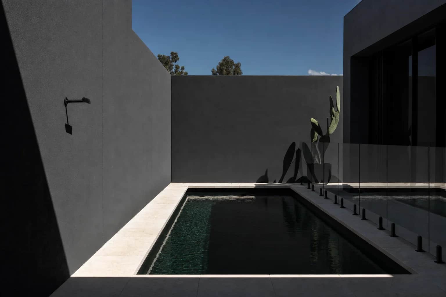Pale stone coping around a dark bottomed pool against a charcoal rendered wall