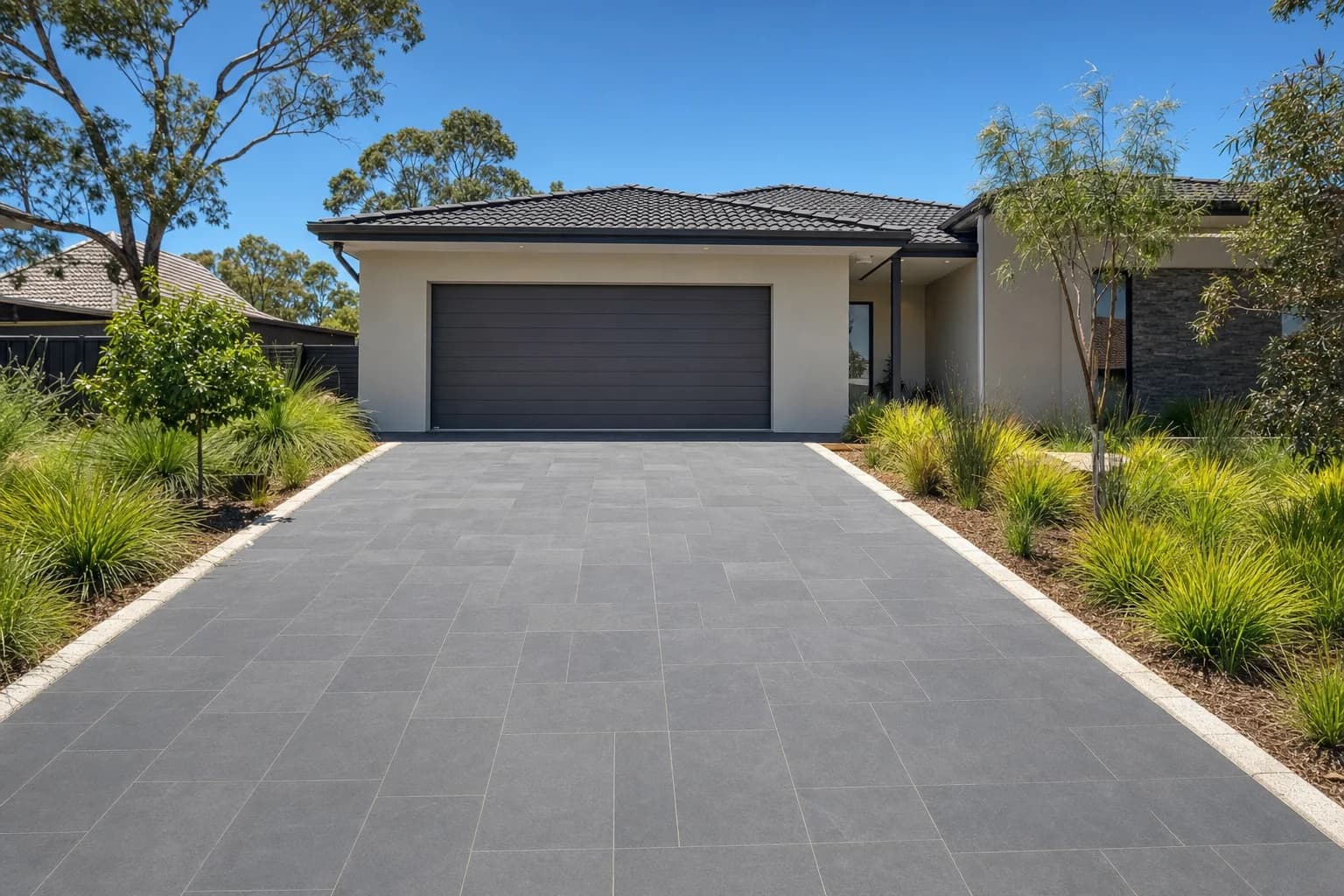 A driveway of large format charcoal stone pavers running from the street kerb to the garage of a rendered Perth home