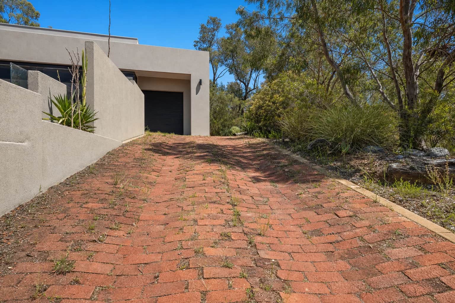 An old brick driveway sunk into two shallow ruts along the wheel tracks with weeds through the open joints