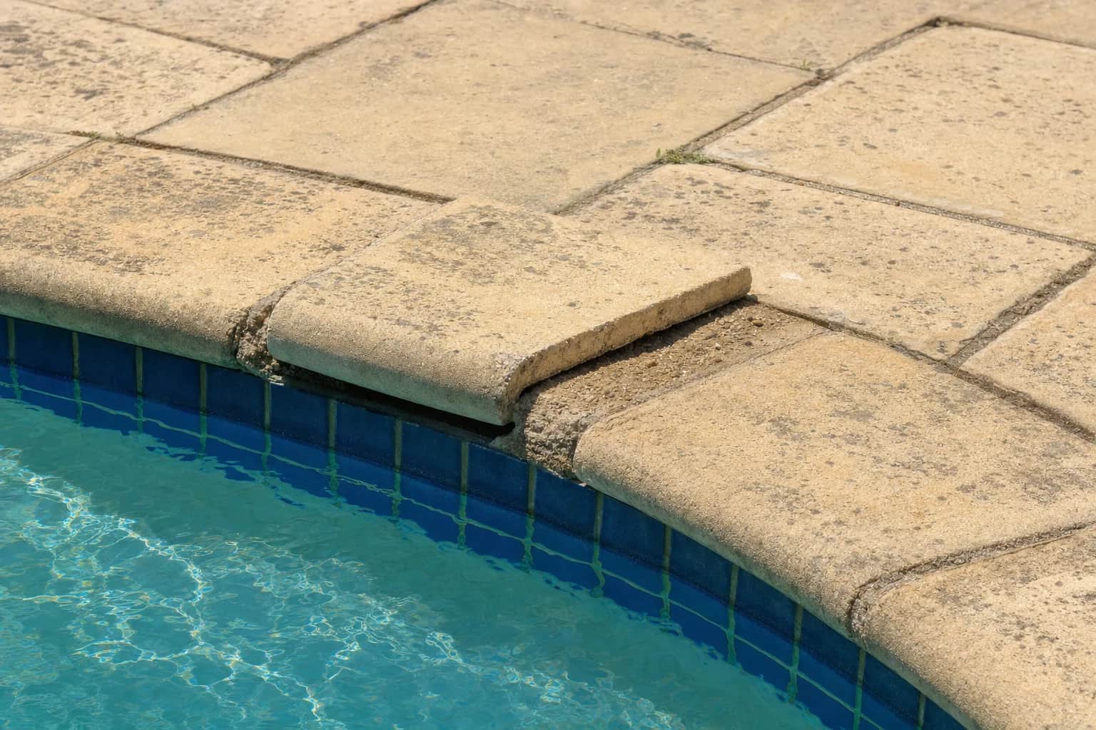 A lifted coping stone sitting proud of its neighbours with the joint washed out beside it