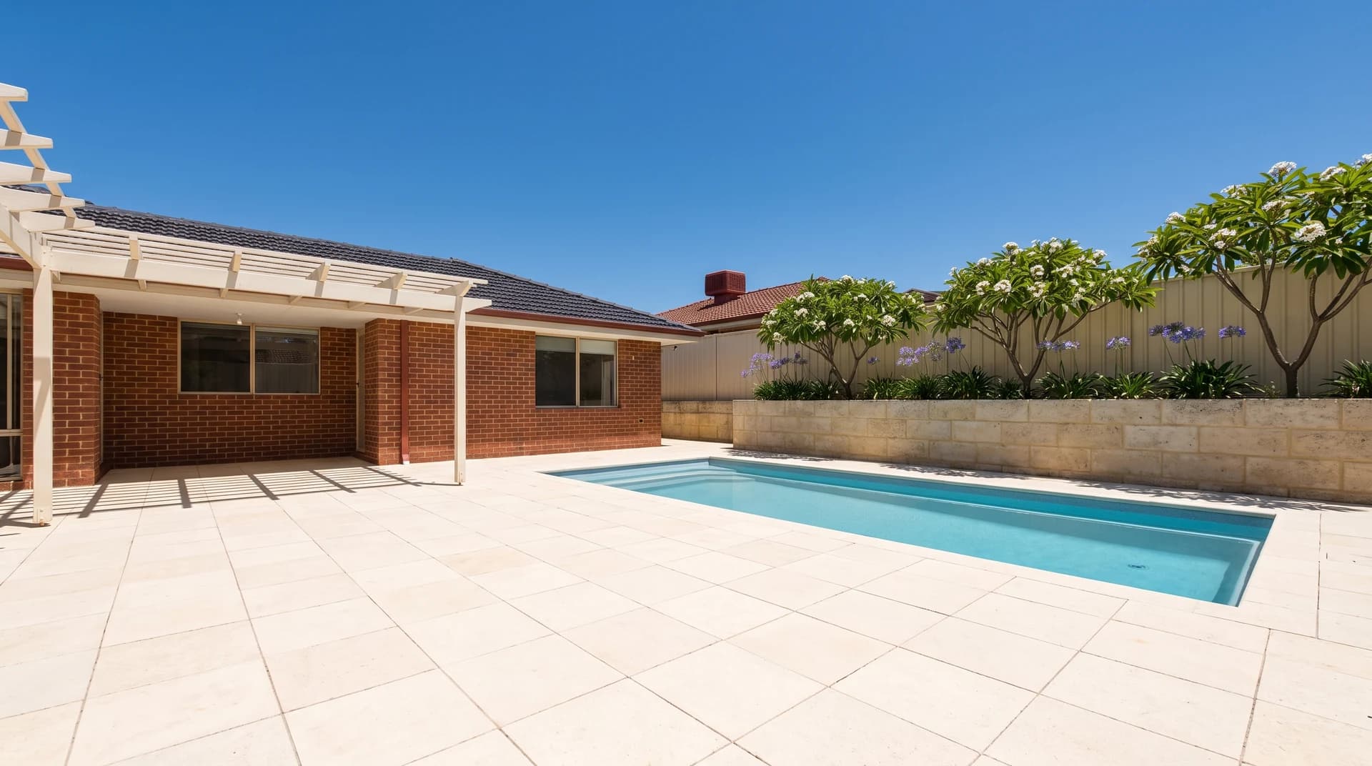 Pale reconstituted limestone paving across a Perth pool surround and alfresco beside a limestone block retaining wall