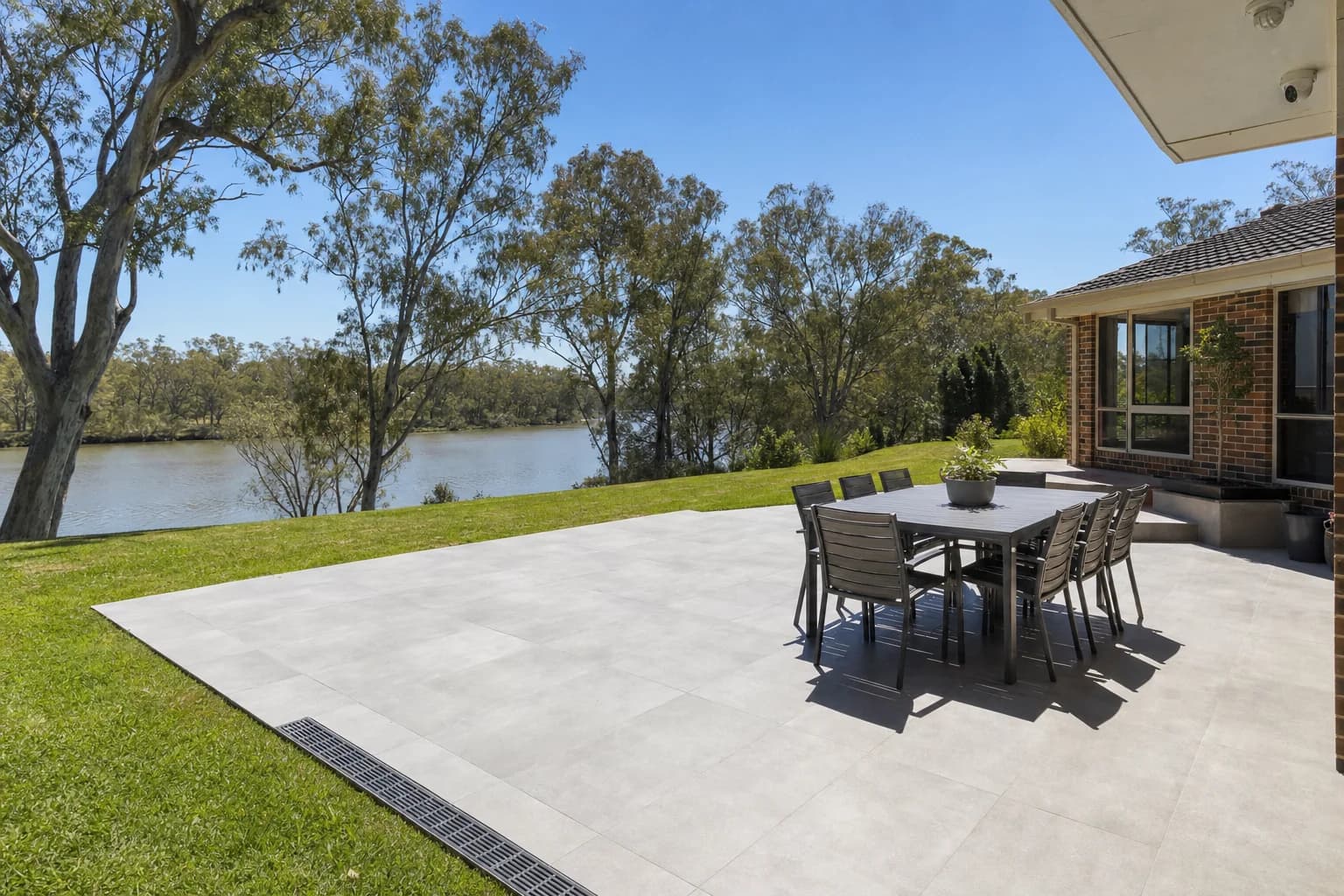 A wide porcelain alfresco area in Applecross with a slot drain along the lower edge and the river through the trees beyond