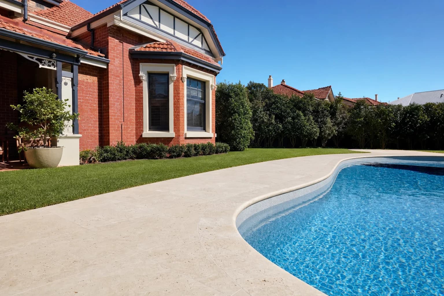 A narrow travertine pool surround with a bullnose coping edge curving around the pool at a Claremont home