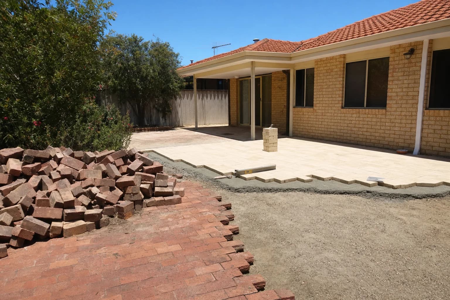 A Currambine backyard part way through a paving replacement, old clay brick paving lifted and stacked and new pavers going down on a mortar bed