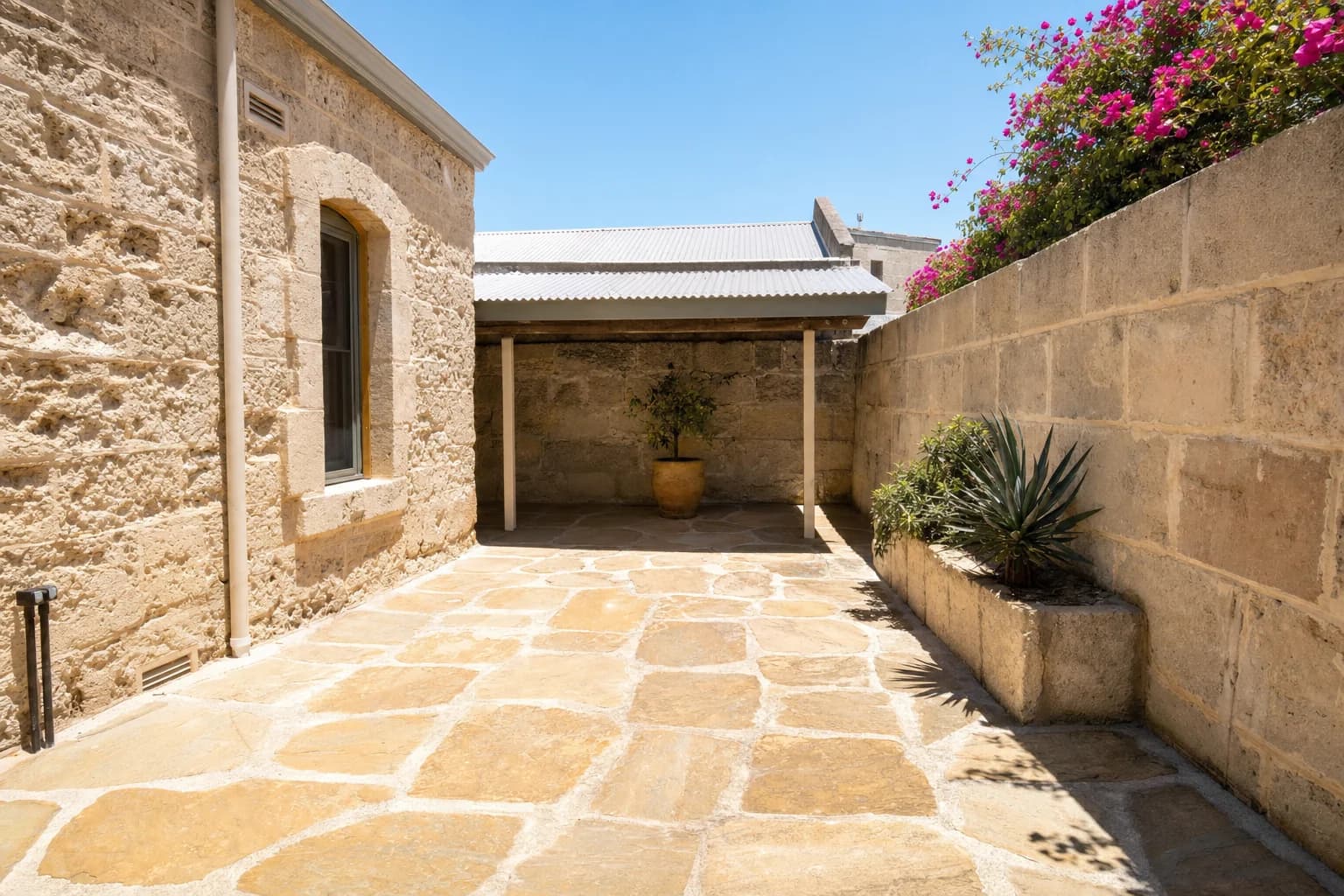 A walled limestone flagstone courtyard behind an old Fremantle cottage, rough limestone block walls either side