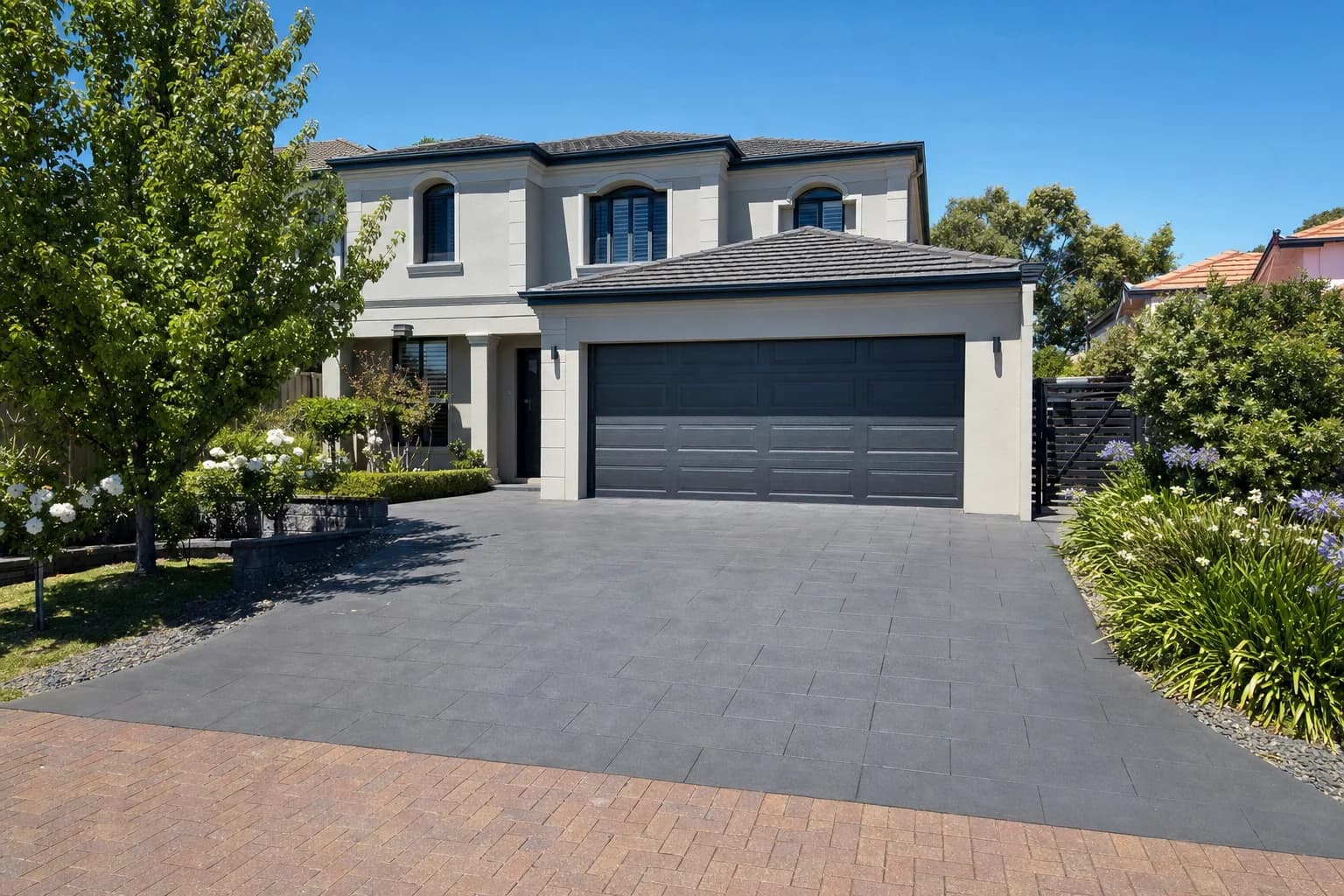 A wide Joondalup driveway paved in large-format charcoal pavers running from the street to a double garage