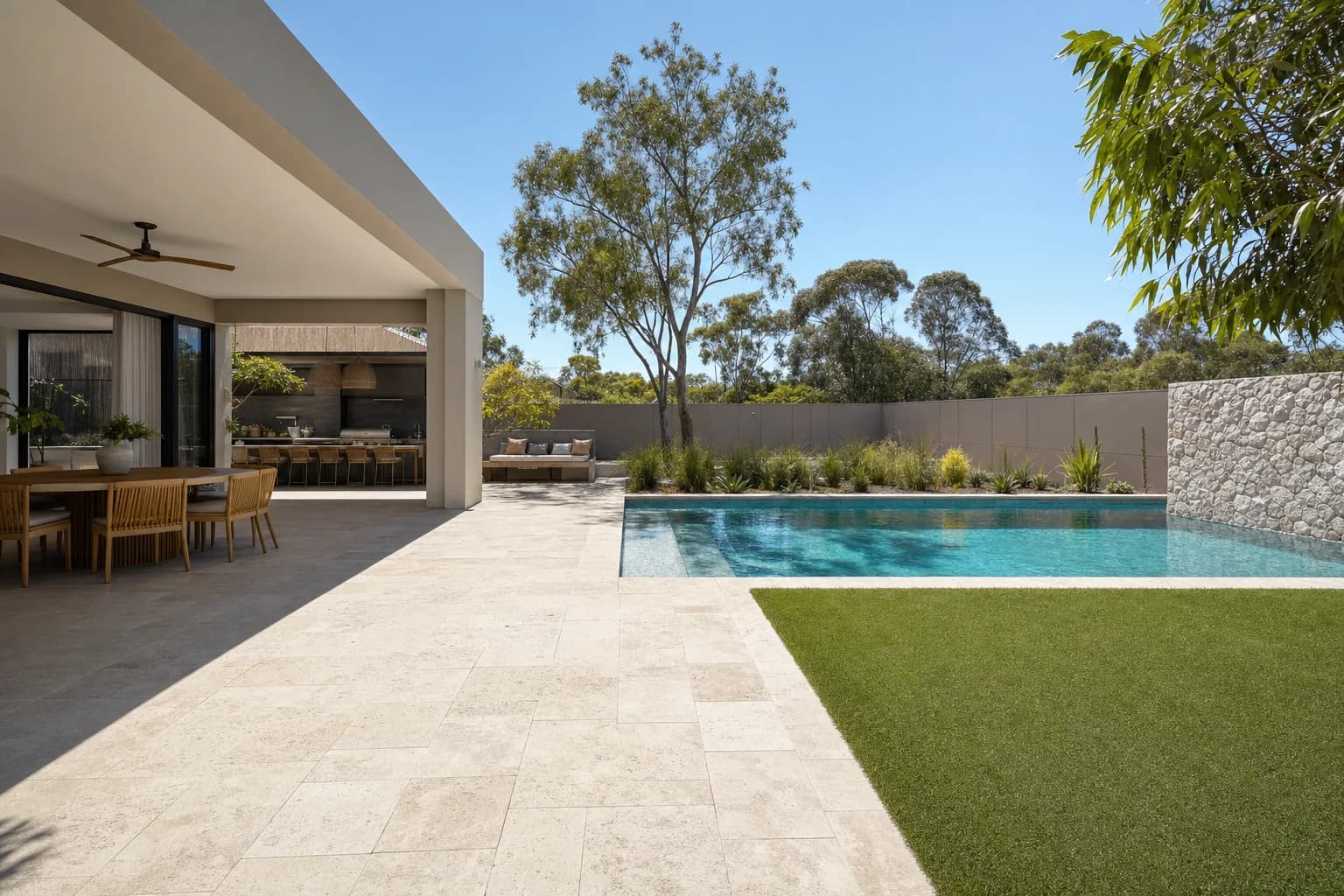 Travertine paving running from a covered alfresco past a swimming pool and out to a lawn as one continuous surface