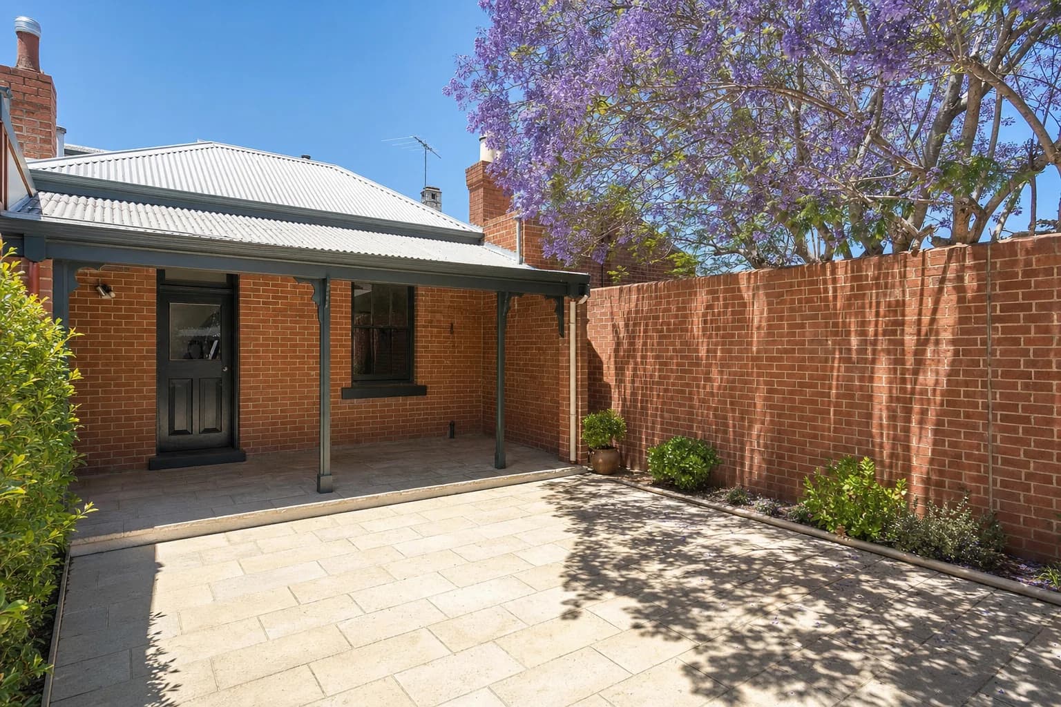 A small paved rear courtyard behind a Subiaco character cottage, cream limestone flagstones under a jacaranda