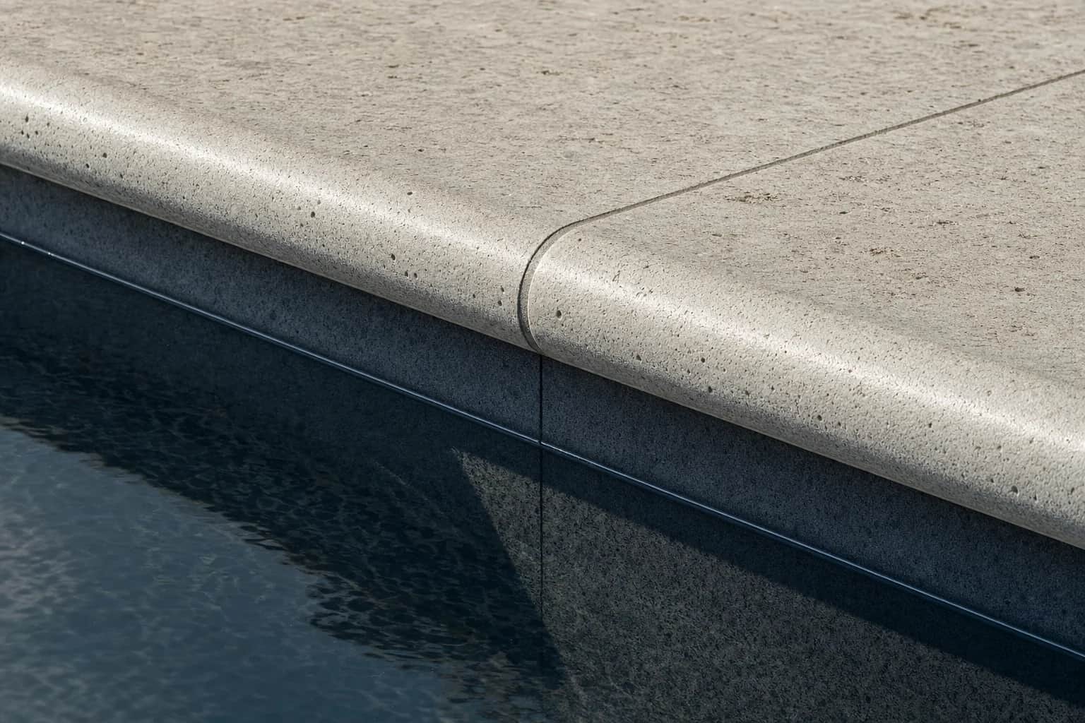 Detail of a rounded bullnose coping profile meeting still pool water