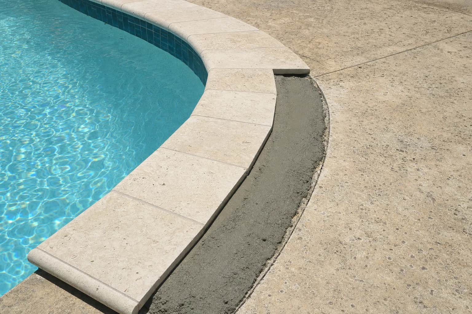 A pool coping replacement part way through, new units set on one side and a fresh mortar bed exposed alongside