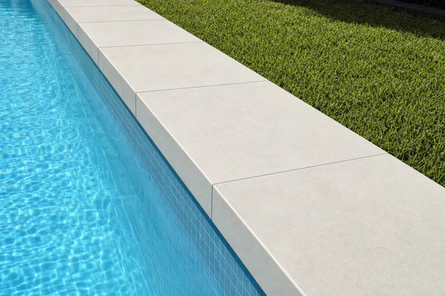 Sharp square edged pale porcelain coping running along the straight side of a lap pool