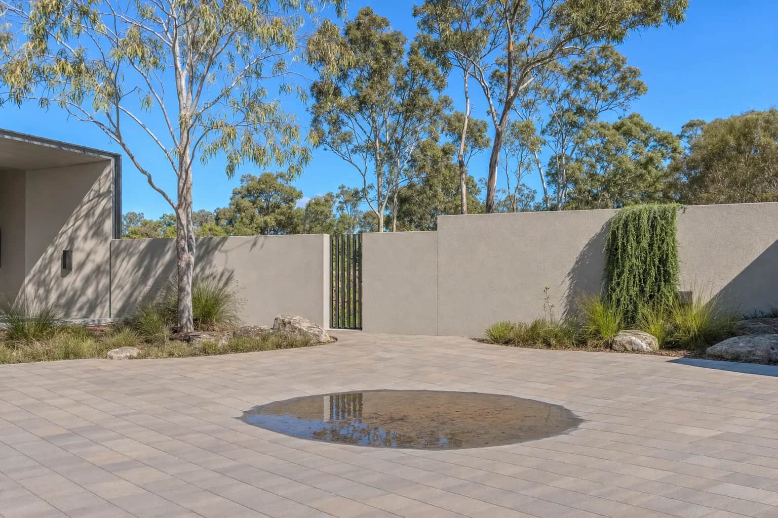 A shallow dished depression in a paved courtyard holding a puddle of water after rain