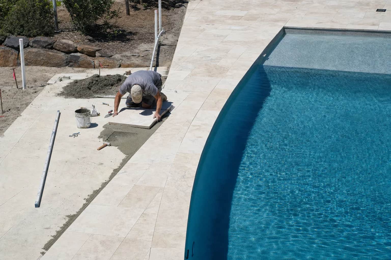 A paver bedding stone beside a pool, seen small in a wide view of the finished paving